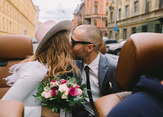 Photo of a bride and groom kissing in the back of a convertible automatible